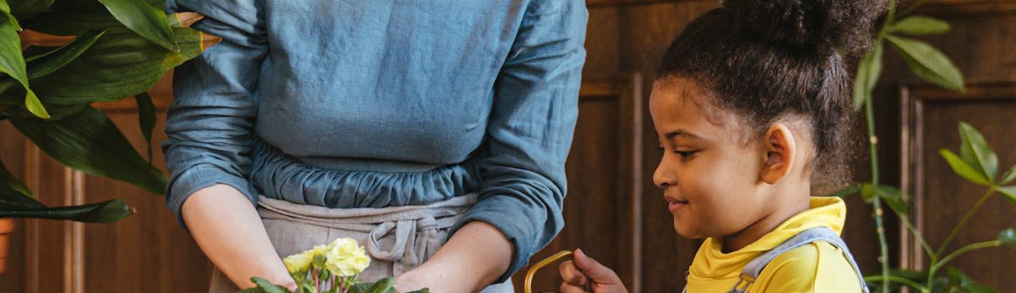 A woman and child bond over gardening with plants and soil indoors.